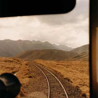 Train tracks disappear over a hill and vanish into a view of rugged peaks, in an image taken from the Observation Car.