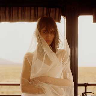 A woman wearing a white slip dress and wind-swept veil leans against the filigree railings on the Observation Car deck.