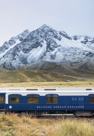 Two white and navy train carriages before snow coated Andean mountains