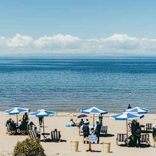 People relax on deck chairs beneath blue-striped parasols on the white sands of Collata Beach by Lake Titicaca's blue waters.