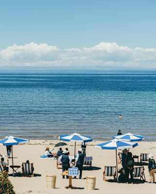 People relax on deck chairs beneath blue-striped parasols on the white sands of Collata Beach by Lake Titicaca's blue waters.