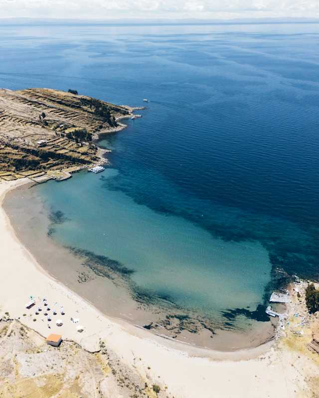 Breathtaking aerial view of the white-sand sweep and clear blue waters of Collata Beach on Lake Titicaca's Taquile Island.