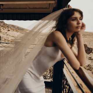 In soft-focus, a bride leans forward on the observation deck rail, propping her chin in a hand as she gazes at the landscape.