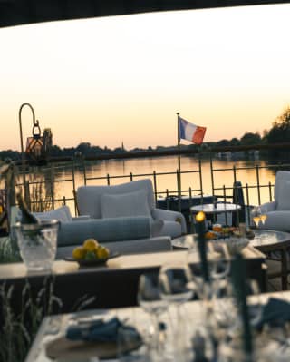 Looking over a dining table in soft-focus to the seating area, where a small French flag flies against the peachy sunset sky.