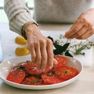 Chef Dominique Crenn prepares a salad of sliced ripe beef tomatoes sprinkled with herbs, seen in close-up.