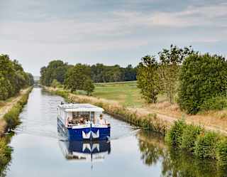 The white and blue Lilas barge cruises one of the peaceful waterways in France's Burgundy region, surrounded by nature.