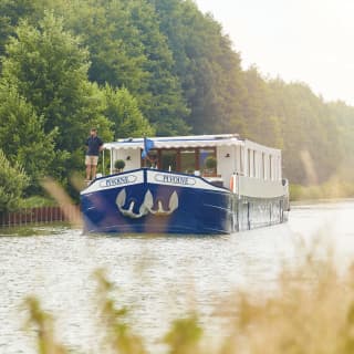 Blue bottomed luxurious river barge sailing along a tree-lined river