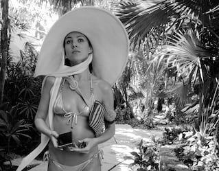 Mulher com traje de banho e chapéu grande passeando por um jardim
