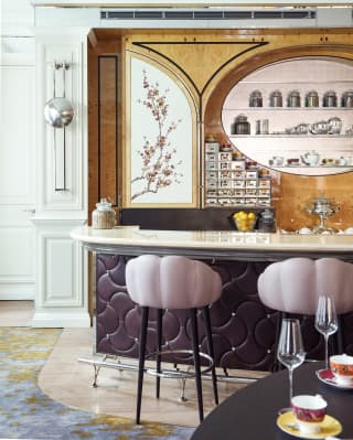 Two dusky pink stools under a marble bar top with tea pots in an oval shelf above