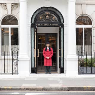 Smiling doorman in a red-coat under a black arched ironwork door