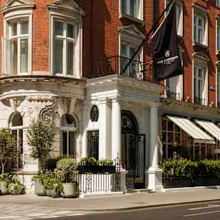 Corner view of The Cadogan Hotel where a branded black flag hangs above the portico entrance set into its Queen Anne façade.