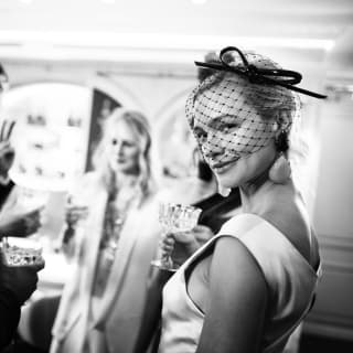 A woman in a light satin dress and dark net veil smiles at the camera in this black and white image of a vibrant party
