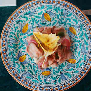 Looking directly down on charcuterie ball topped with a crisp and served on floral turquoise and orange ceramic plate.