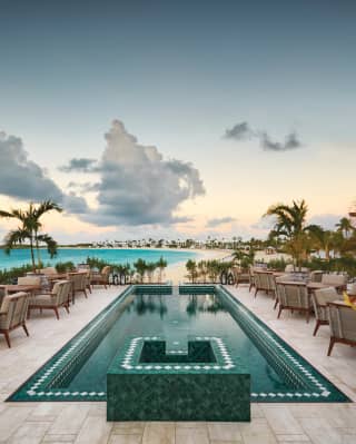 A long and narrow pool tiled in emerald green points to the beach, flanked by rows of rosewood tables and cushioned armchairs
