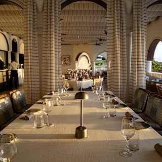 View down a table with two lamps, plates, napkins and wine and water glasses, in a restaurant with elegant neutral décor.