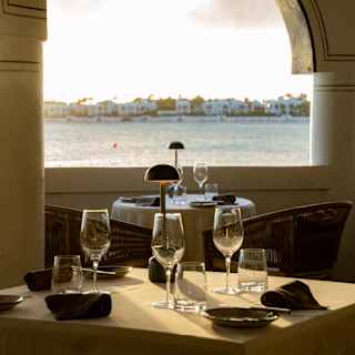 Eye-level view over a dining table with three wine and water glasses, to a wall arch framing a moody Maundays Bay vista.