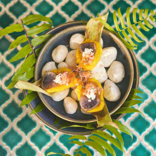 Looking down on a dish of Panquitas, with cream and chalaquita salsa, served on white stones, at a teal-tiled table top.