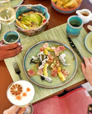 Guests enjoy vibrant Peruvian dishes at Uchu, seen from above a diner who holds a cocktail with a foam and citrus garnish.
