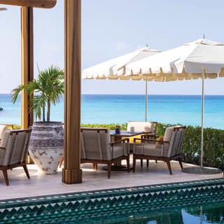 Restaurant table under a white parasol beside an outdoor pool lined with jade-coloured tiles