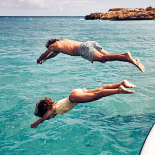 A couple diving into clear turquoise water from a boat