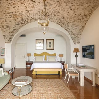 Polished russet floor tiles reflect a butter yellow vallance, crisp white linens top a king bed near a gilt edged white chair
