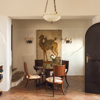 A large Renaissance-style camel painting dominates the whitewashed stone wall of a Neapolitan furnished dining room
