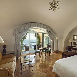 Sunlight plays across polished floor tiles while theatre-style curtains frame a glorious balcony view of the Tyrrhenian Sea