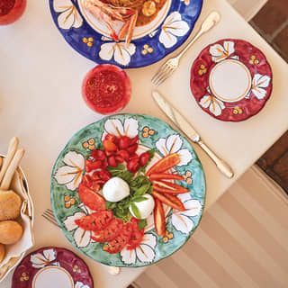 Hand painted plates carry antipasti of mini mozzarella balls, cherry and beefsteak tomatoes, and fresh basil leaves