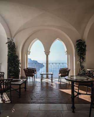 Bar tables on an open-air stone terrace with arched windows overlooking the Amalfi Coast