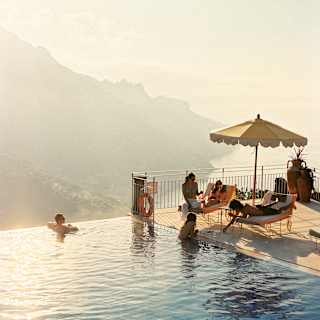 Two guests swim in the gold-tinted waters of the pool as they chat to three more who relax on loungers, seen from above.
