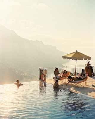 Two guests swim in the gold-tinted waters of the pool as they chat to three more who relax on loungers, seen from above.