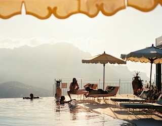 Two friends relax in the pool and chat to three more who sit on loungers enjoying the views and perks of the La Piscina club.