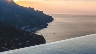 View over an outdoor infinity pool of coastal towns along a shoreline at sunset