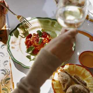 Seen from above, a guest raises a glass of white wine above a vibrant plate of spaghetti Ravello with tomatoes and basil.