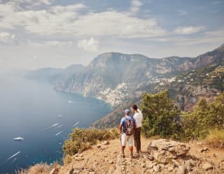 Couple standing on a rocky cliff top gazing across the coastal waters below