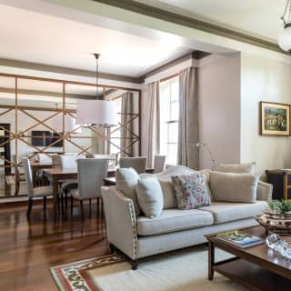 A light, spacious and luxurious hotel suite with sofa in the lounge, dining table for six and screened bedroom area beyond