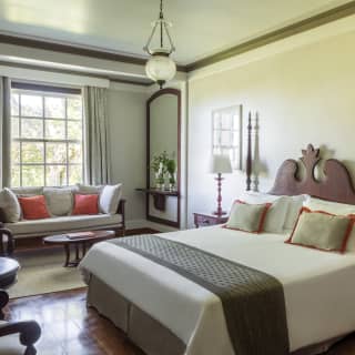 Sunshine floods through a sash window into a neutral-coloured suite with immaculate double bed, tiled floor and elegant sofa