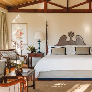 A large luxurious terrace suite bed under a gently pitched ceiling with sunlight shining across the polished wood floor