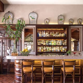 Three yellow leather bar stools at a marble bar top, with liquor on shelves behind