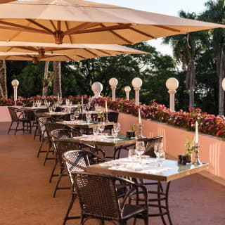 Tables set for two on the outside terrace of Itaipu Restaurant under large sun shades with views of lush palm trees