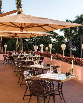Tables set for two on the outside terrace of Itaipu Restaurant under large sun shades with views of lush palm trees