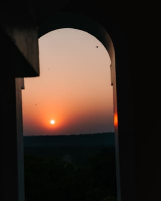 A setting sun glows bright in the darkening peach and purple sky, seen through an arch in the hotel's Colonial-style tower.