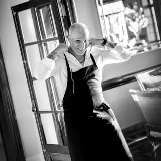 Black and white image of Chef Luiz Filipe Souza smiling to camera as he adjusts his apron in the doorway of Restaurant Y.