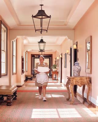 Housekeeper carrying linen along a pink sunlit corridor