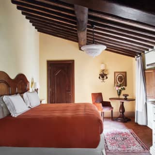 Rustic hotel room with a terracotta-coloured king bed and wooden beamed ceiling