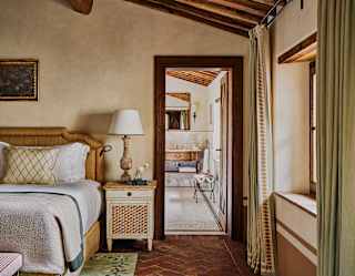 View from the country-style bedroom through a doorway into the cool Tinaia Suite bathroom with white mosaic tiles and marble.