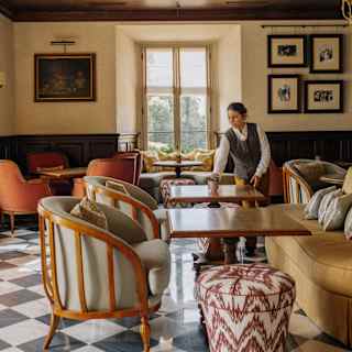 A waitress adjusts a table in the elegant Bar Visconti, with monochrome tiled floor, wood-framed tub chairs and sofas.