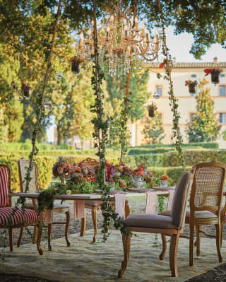 Red-patterned chairs around a floating al-fresco table under a crystal chandelier