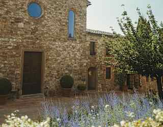 Front view of Chiesa di San Tommaso with a wooden door and round window set in ancient stone, seen over a white shrub.