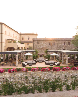 Two L-shaped pergolas offer shade for neatly arranged dining tables set on a spacious raised terraced framed by pink blooms